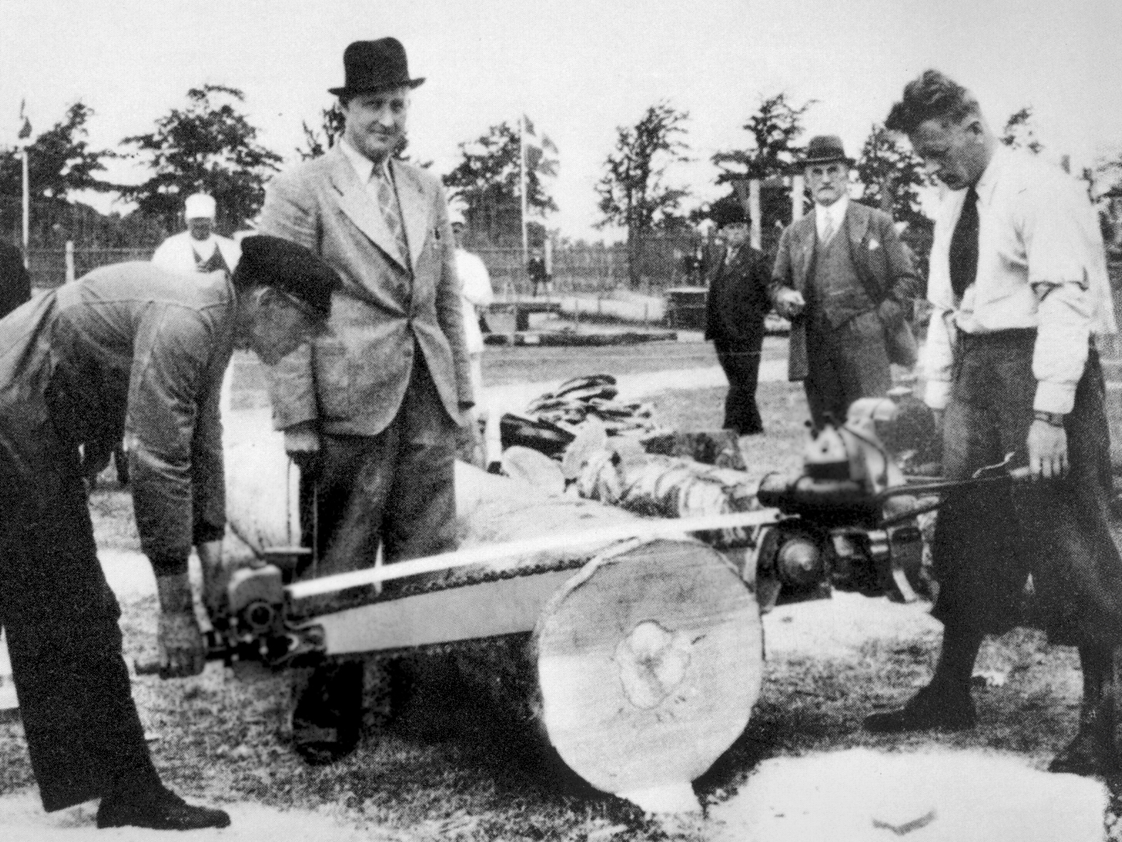 Two men slicing a tree trunk with a STIHL gasoline chainsaw; black and white photo.
